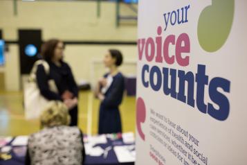Poster saying "Your voice counts" and two people talking in the background