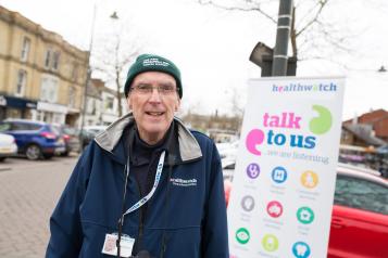 Volunteer standing infront of a banner that says 'talk to us'