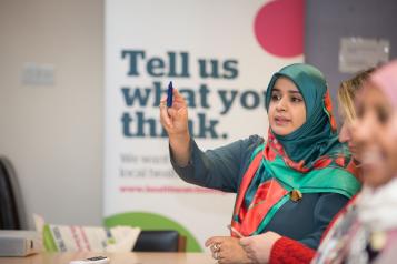 Woman in headscarf putting her hand up at Healthwatch event