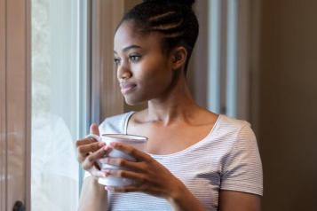 A woman looking sad, looks out of the window holding a cup of tea