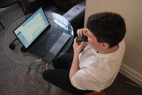 A young person with a visual impairment say at a laptop.