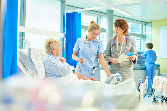 An older lady sat in a hospital bed with a nurse and doctor by her bedside
