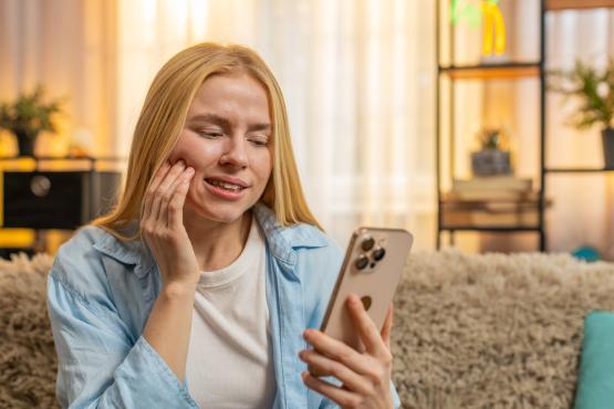 Young woman feeling tooth pain at home, worried face, searching phone for dentist