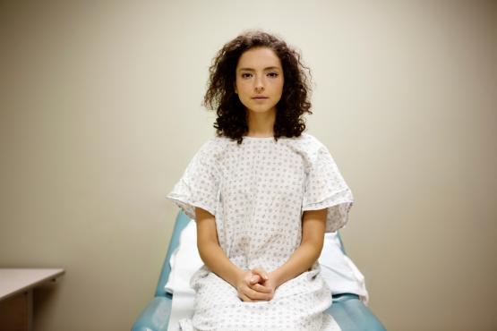 A woman sitting on a hospital bed in a hospital gown.