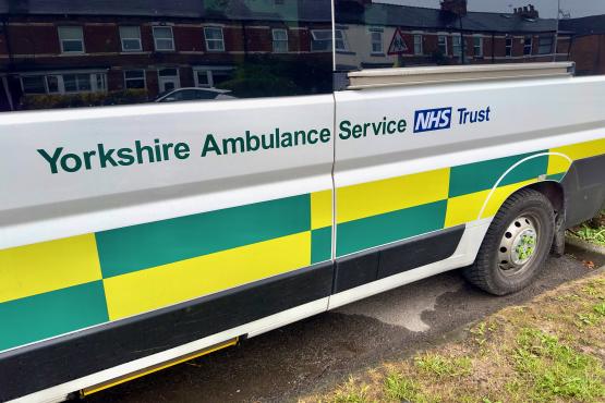 Side view of a Yorkshire Ambulance Service NHS Trust patient transport vehicle parked on a residential street