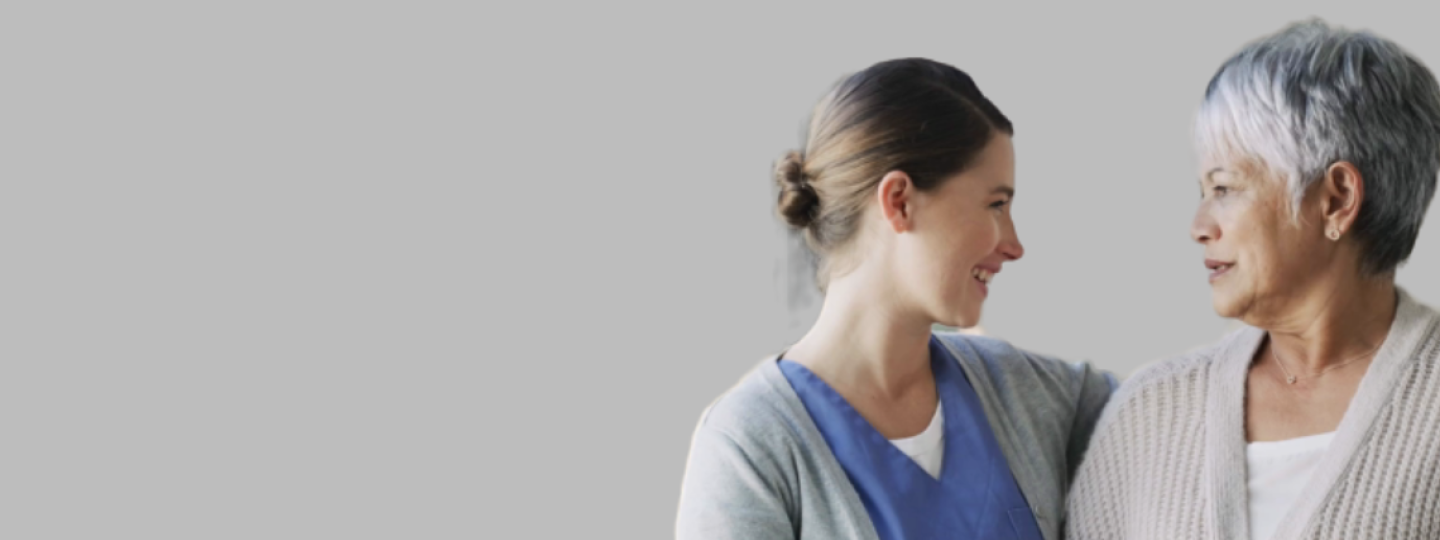 A healthcare assistant and an older lady smiling at each other