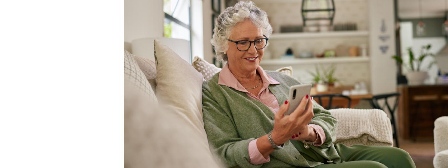 Old casual woman sitting on a couch using smartphone in living room
