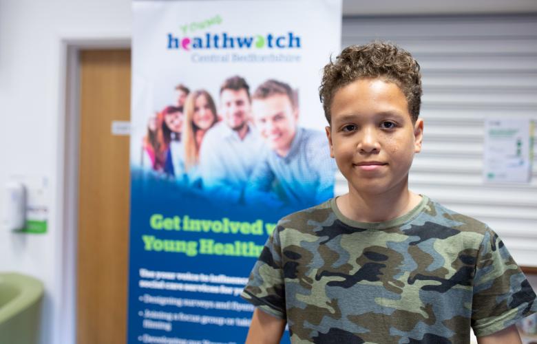 Young male volunteer standing in front of Healthwatch branding
