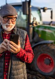 Senior farmer with mobile phone in field with tractor in background