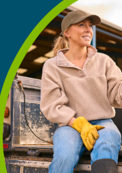 Female farm worker sitting on tailgate of off road farm vehicle with dog