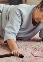 Sick older woman with headache lying on the floor with wooden stick after having a fall.